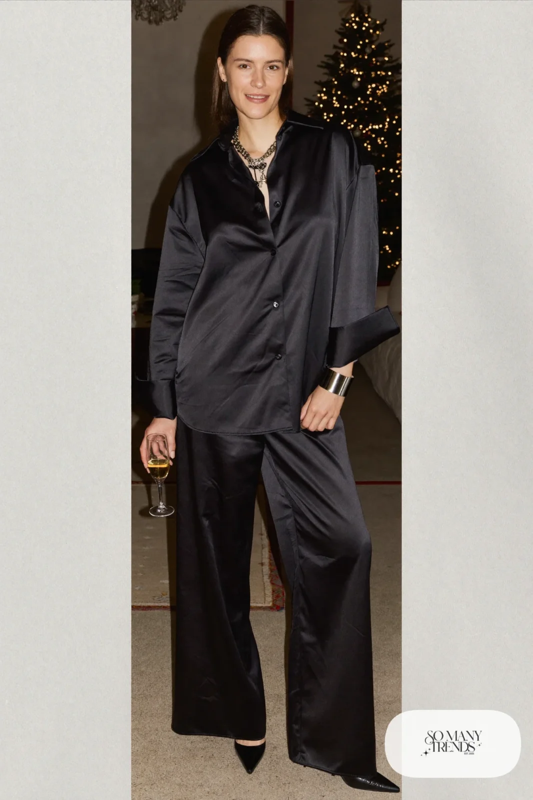 Woman in a black satin pajama style shirt and wide-leg pants with layered silver necklaces and black heels, New Year's Eve outfit 21