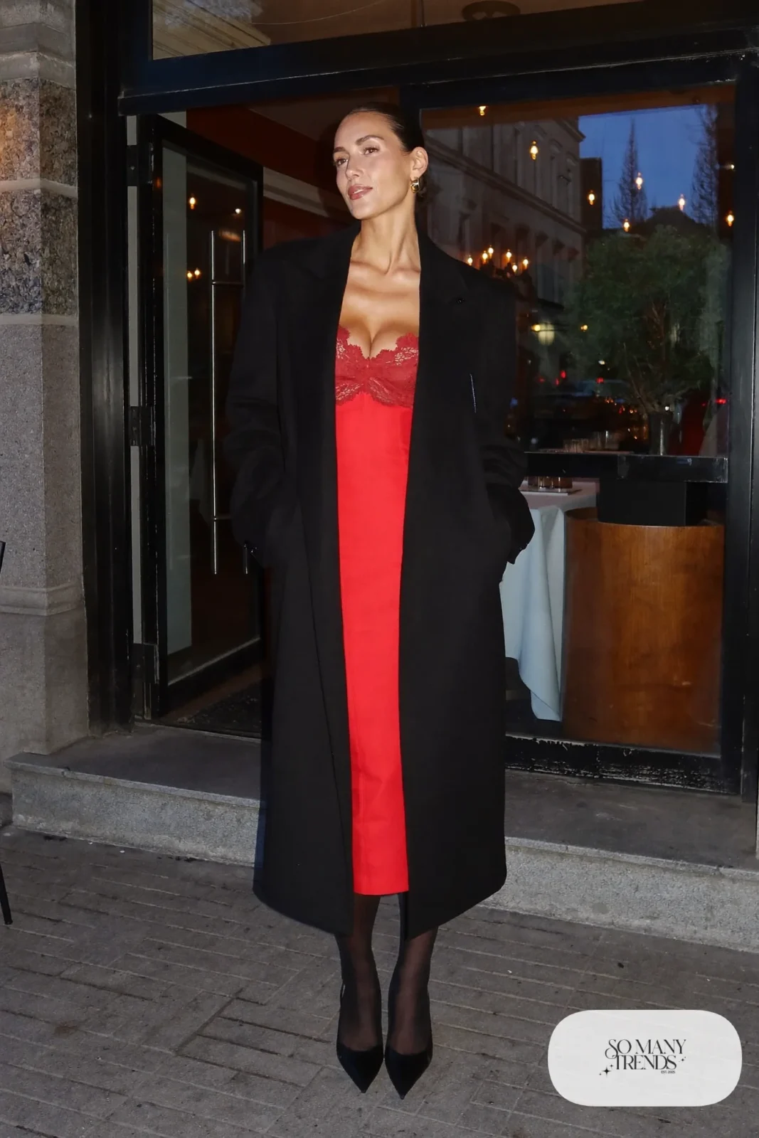 Woman in a fitted red lace-trim midi dress, long oversized black wool coat and black pointed pumps, look 1