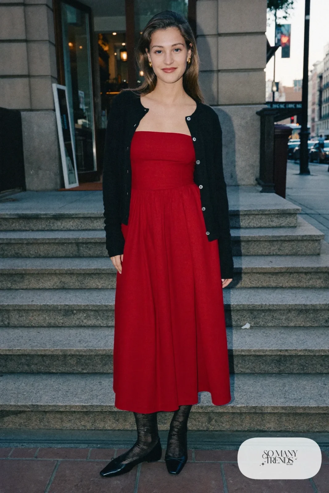 Woman in a red structured bodice midi dress, black cardigan and black ballet flats, look 5