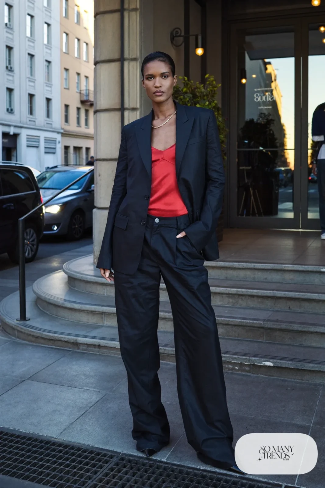 Woman in a black wide-leg pantsuit, red camisole and black pointed pumps, look 13