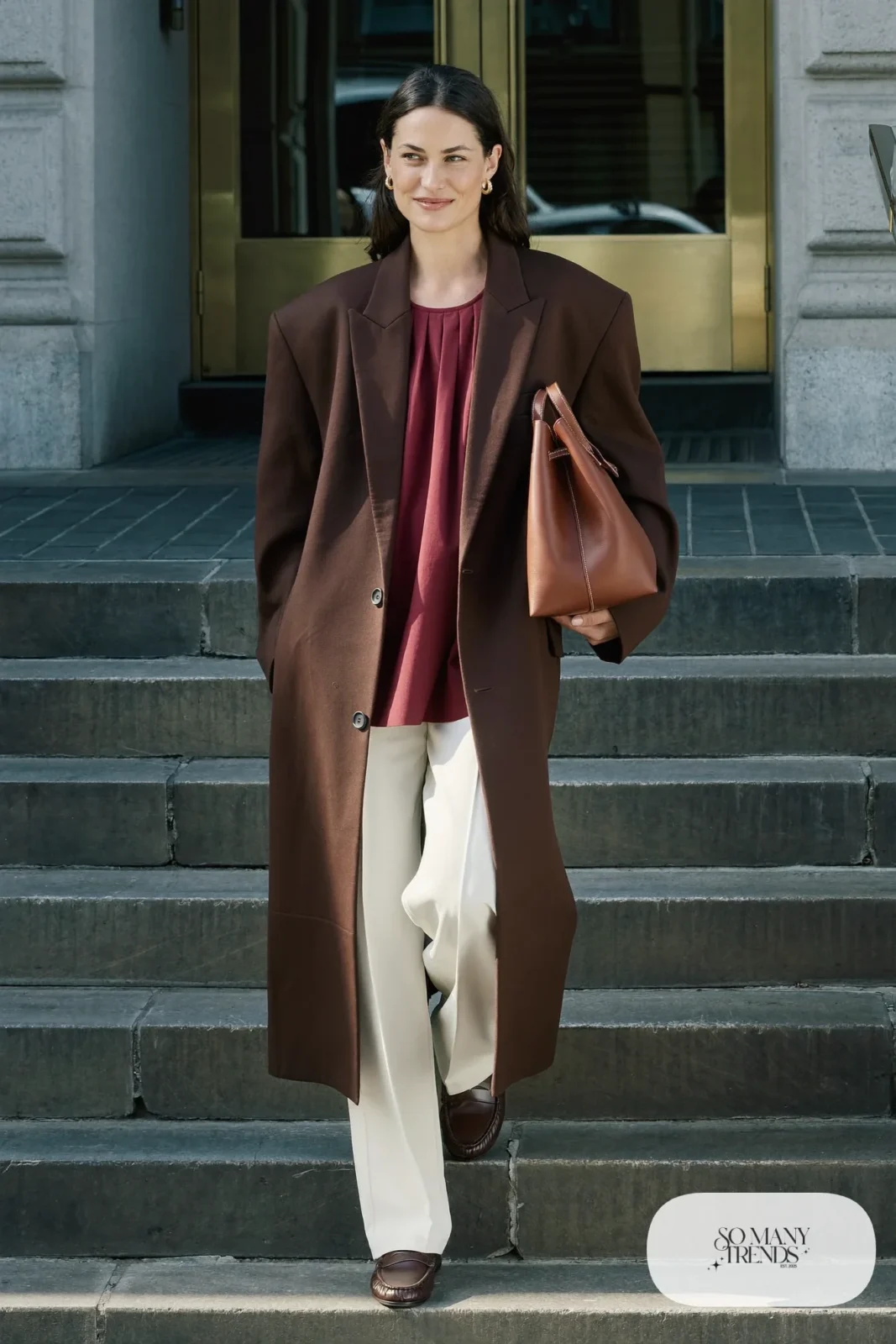 Woman in a long chocolate-brown blazer, burgundy shell top, cream wide-leg pants and brown loafers, outfit 1
