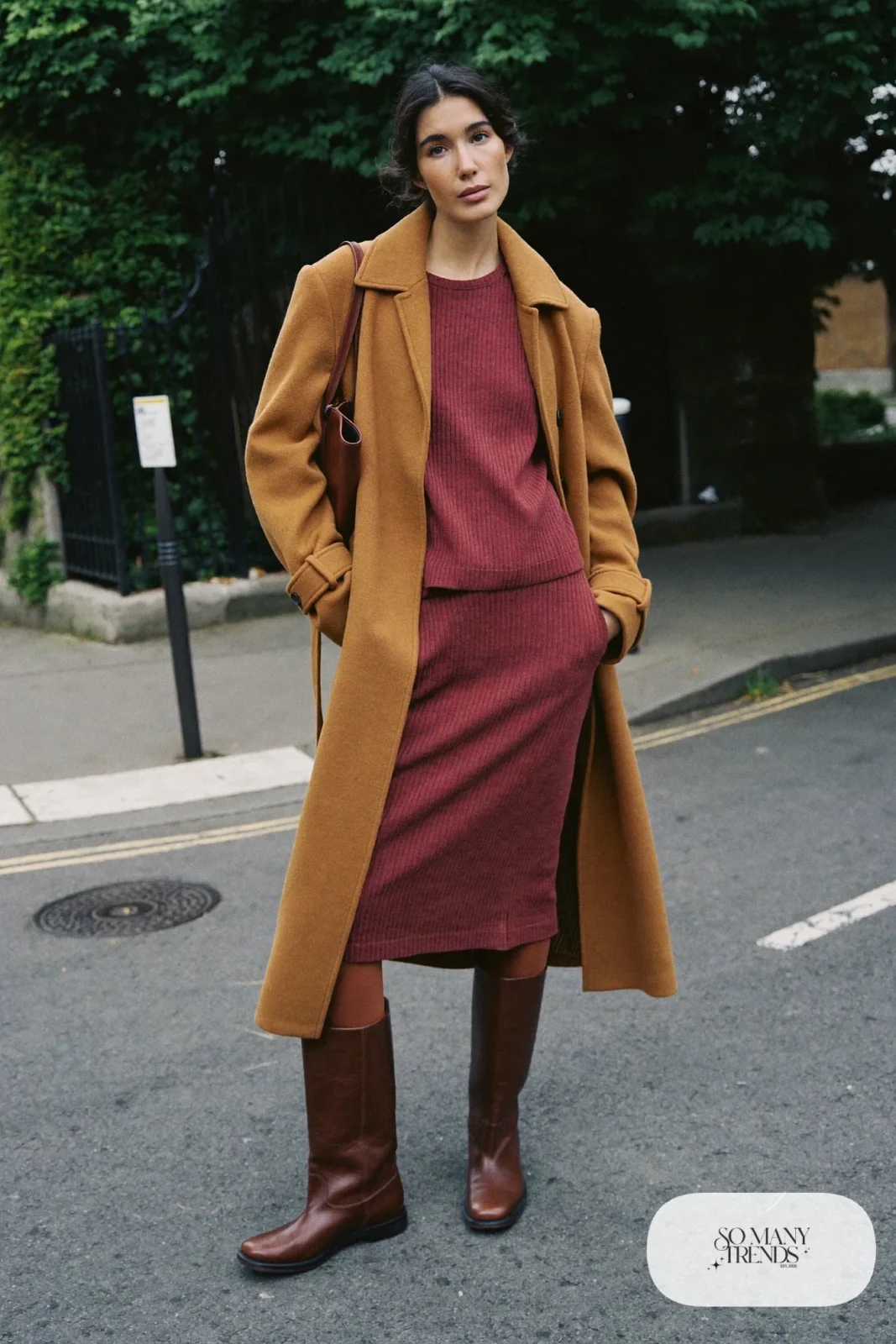 Woman in a burgundy knit midi dress, camel belted coat, tall brown leather boots and brown bag, outfit 2