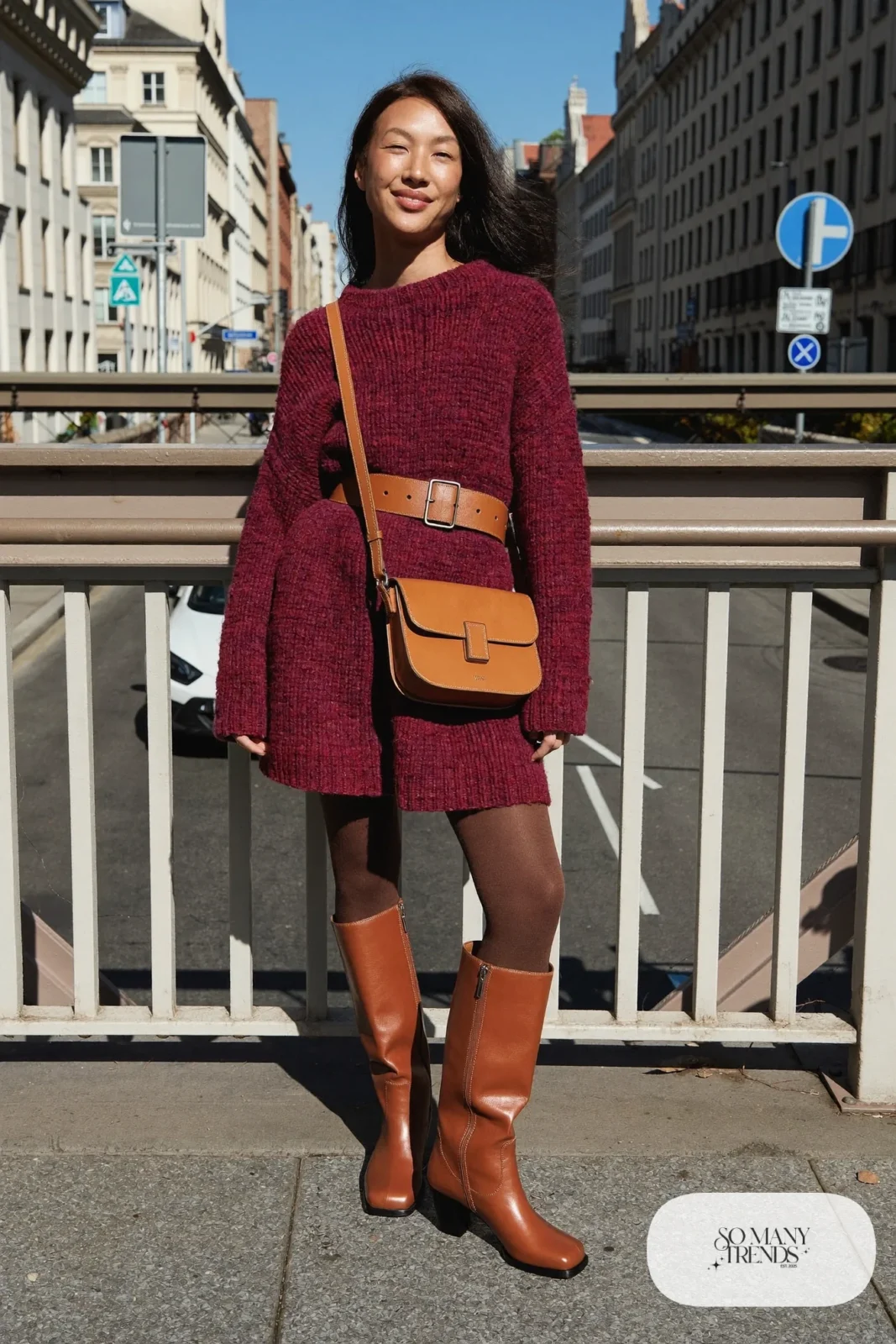Woman in a burgundy sweater dress with a cognac belt and tall cognac boots, outfit 17