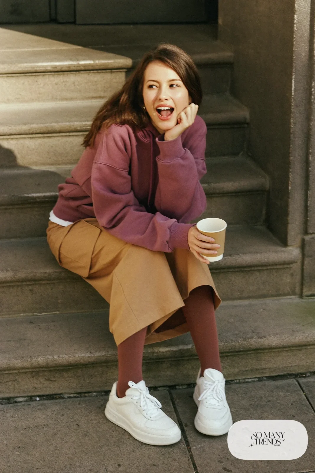Woman in an eggplant heavy cotton hoodie, tan cargo midi skirt, brown tights and white leather sneakers, outfit 27