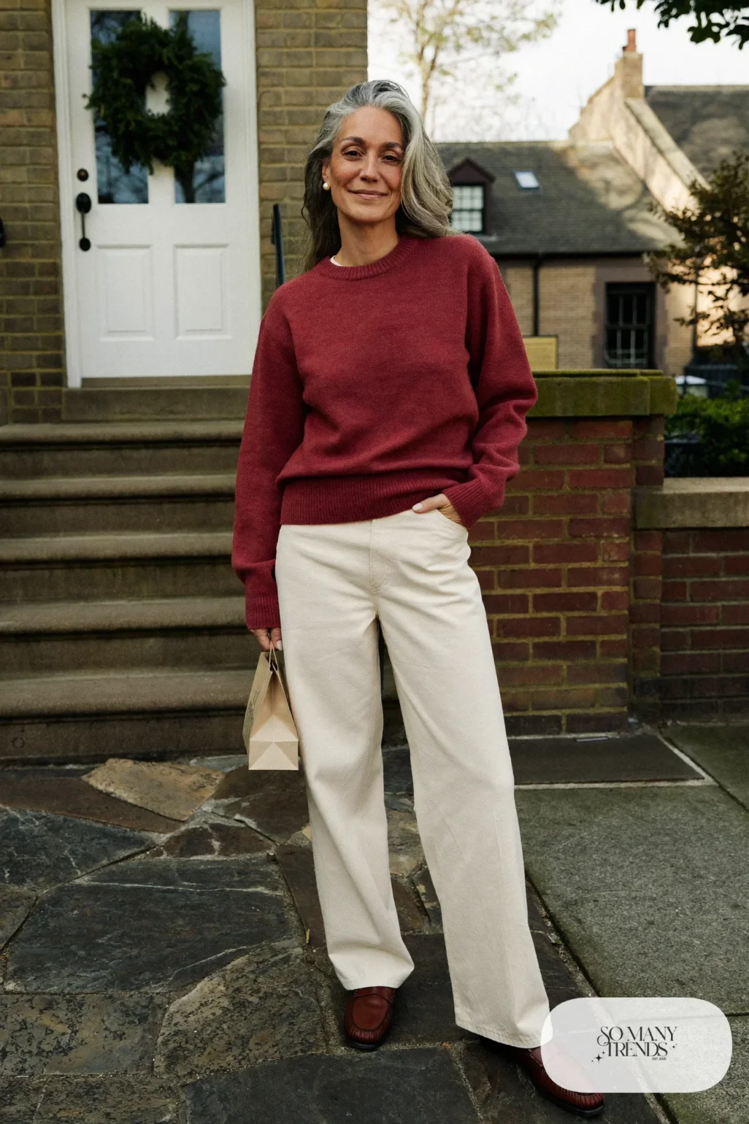 Woman over 50 in an oxblood crewneck sweater, ivory wide-leg pants and brown leather loafers, Christmas outfit 1