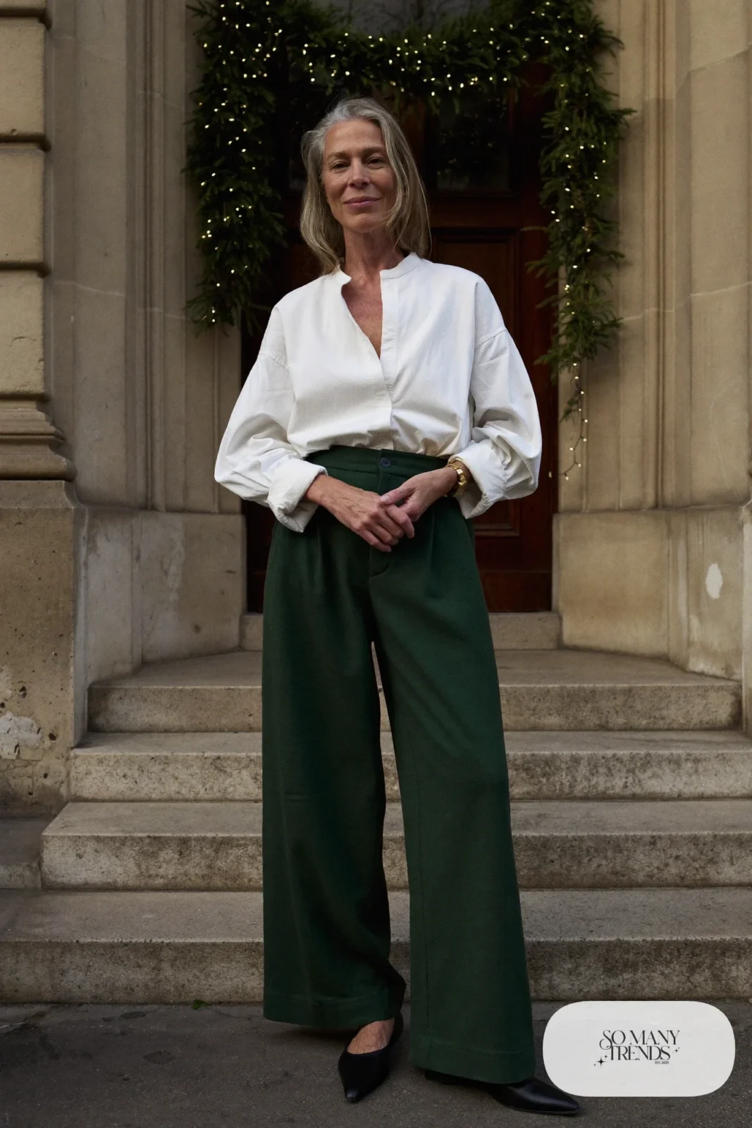 Woman over 50 in forest green wide-leg wool pants, cream button-up blouse and black pointed flats, Christmas outfit 4