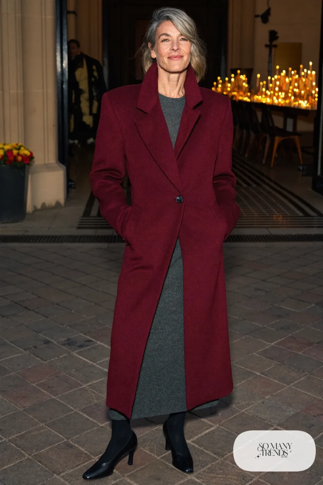 Woman over 50 in a long oxblood wool coat, charcoal knit midi dress, black sheer tights and black block-heel pumps, Christmas outfit 6