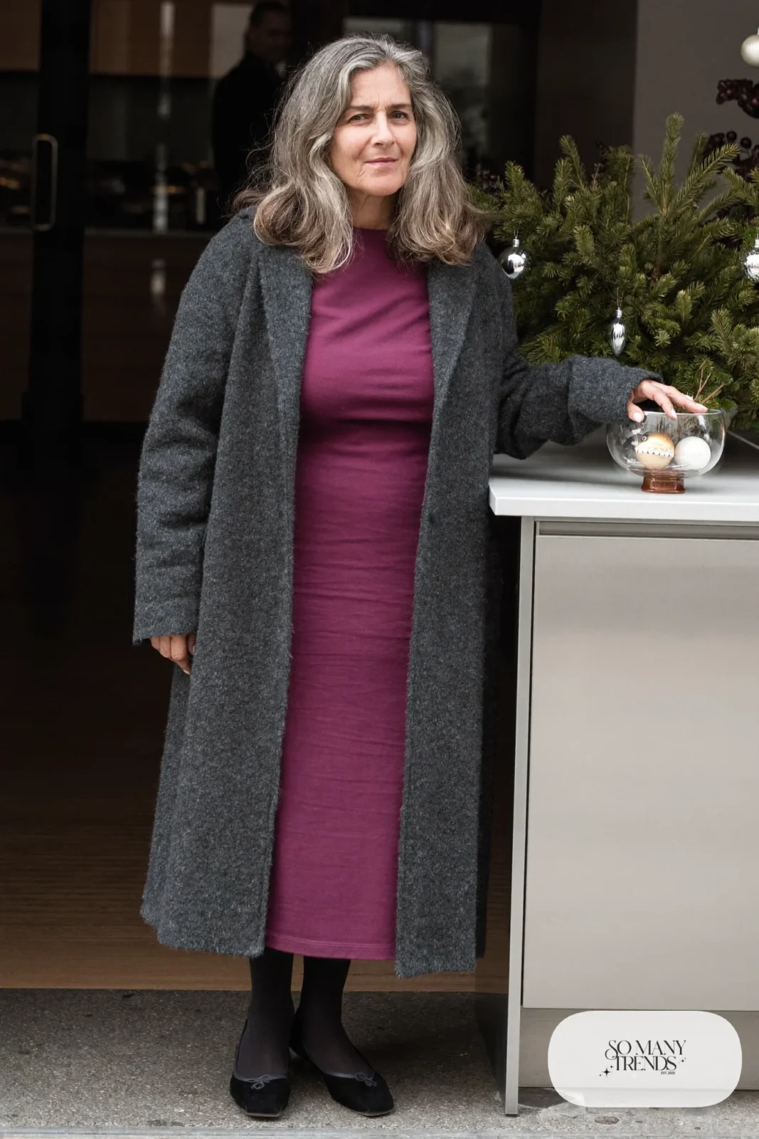 Woman over 50 in a plum jersey midi dress, long charcoal cardigan, black tights and black ankle-strap flats, Christmas outfit 12