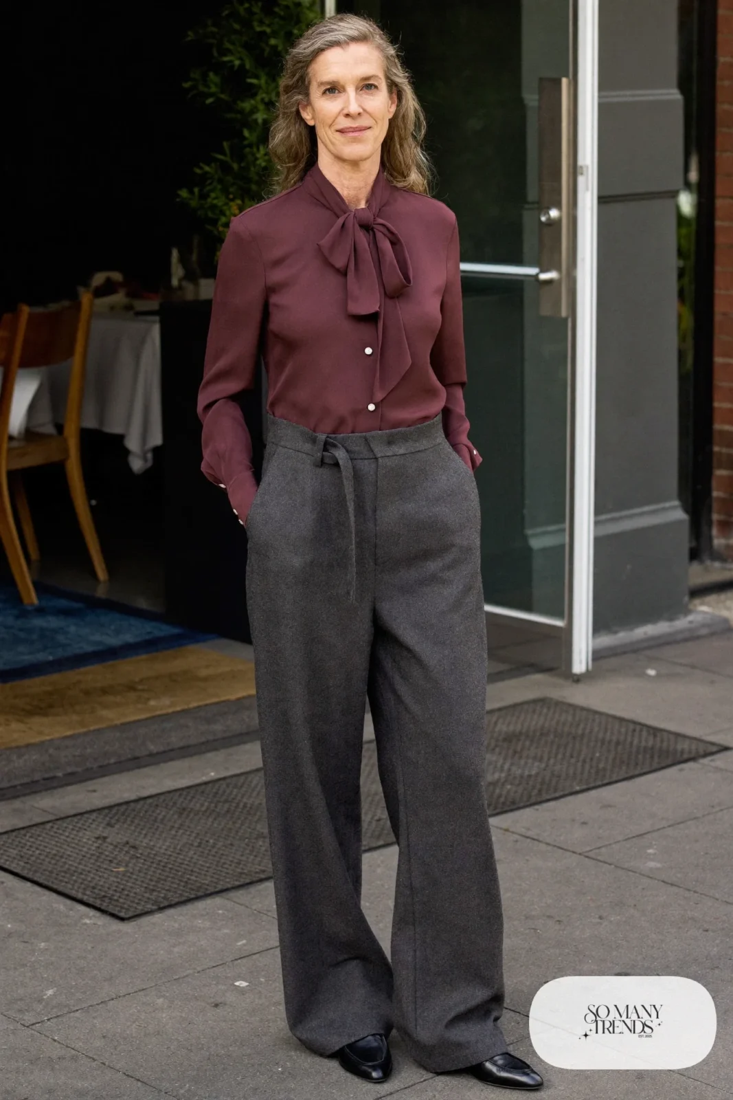 Woman over 50 in a plum crepe bow blouse, charcoal gray flannel wide-leg pants and black loafers, Christmas outfit 18