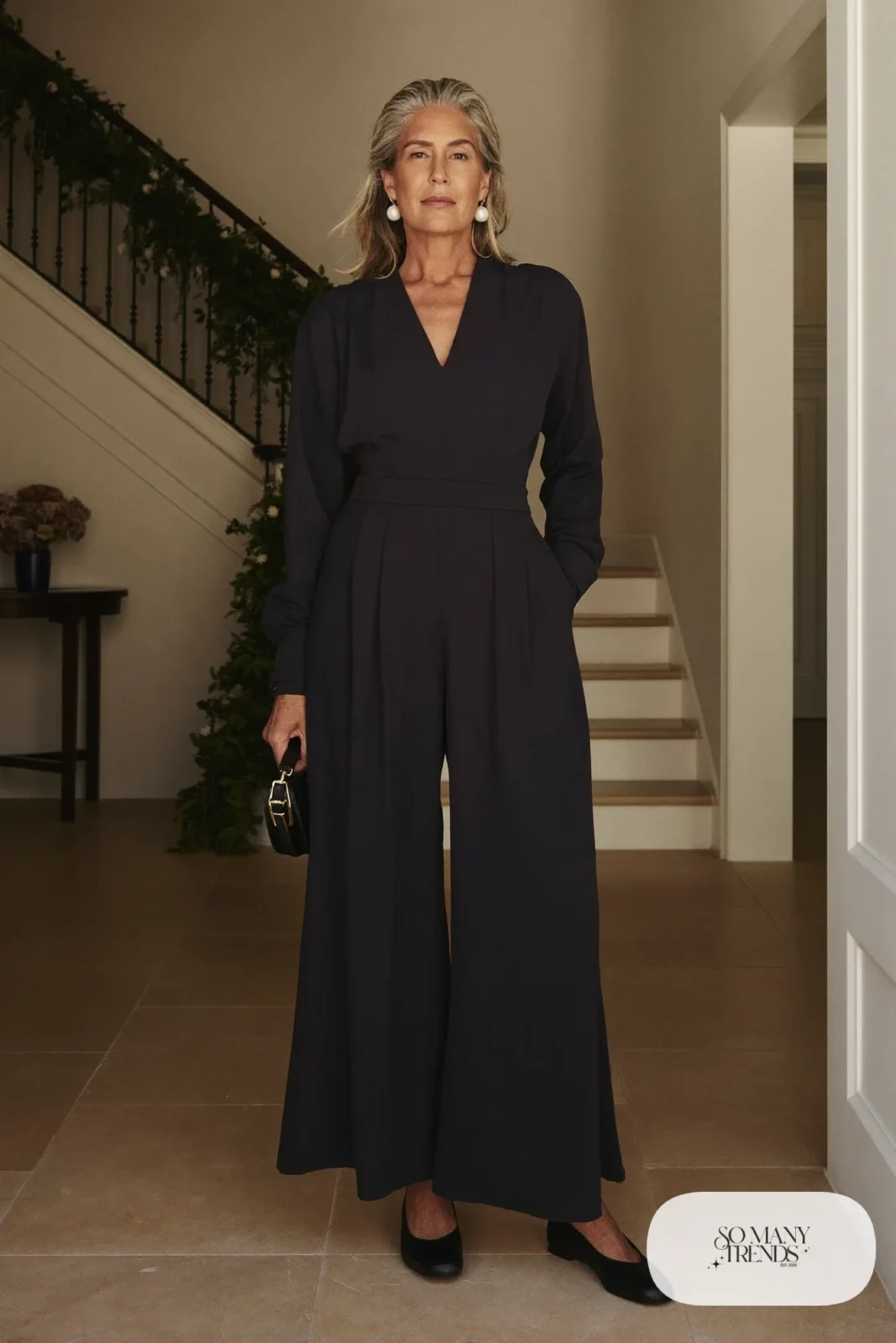 Woman over 50 in a navy crepe wide-leg jumpsuit with pearl earrings and black pumps, Christmas outfit 20