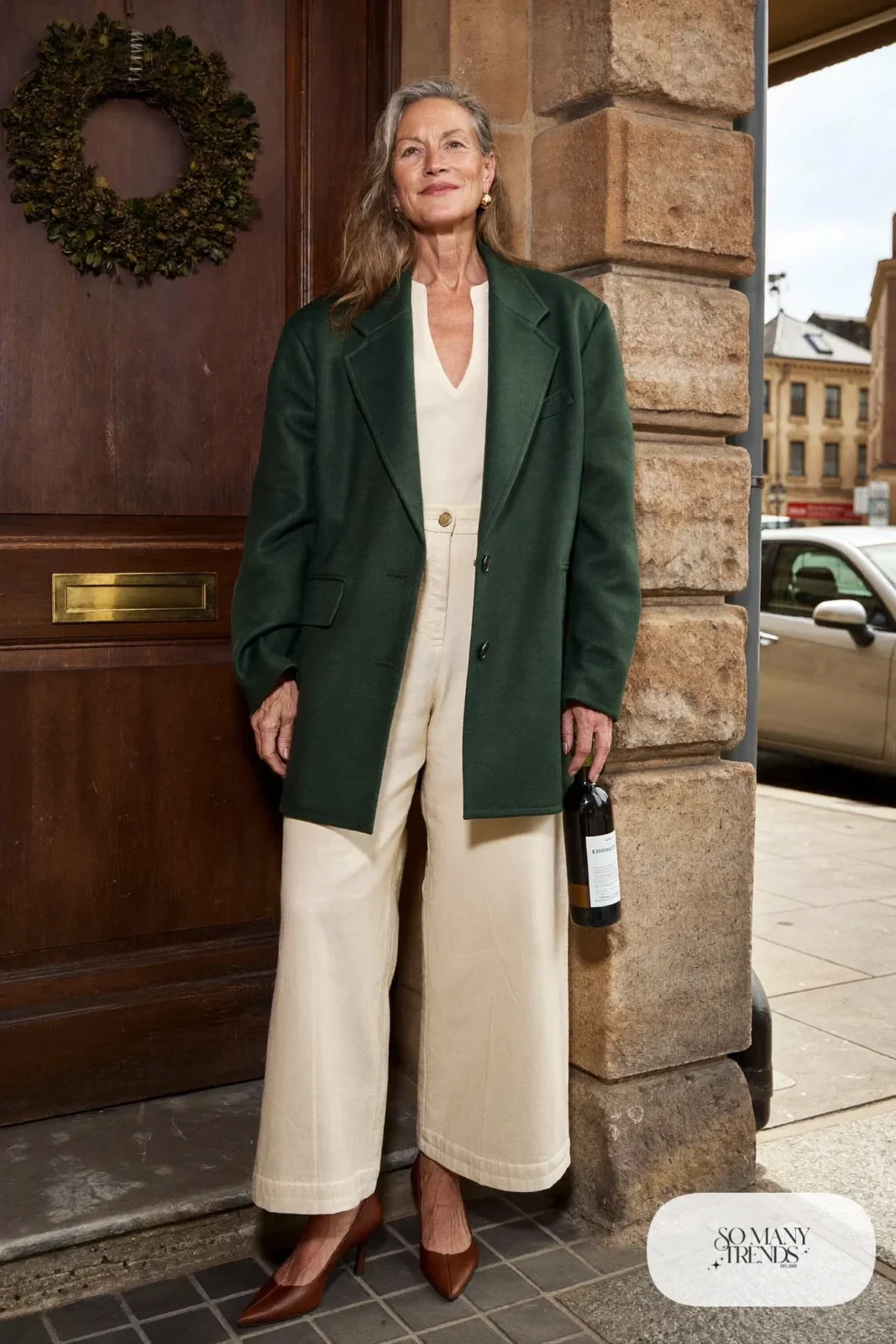 Woman over 50 in a forest green wool blazer, cream wide-leg pants, ivory knit top and brown pumps, Christmas outfit 22