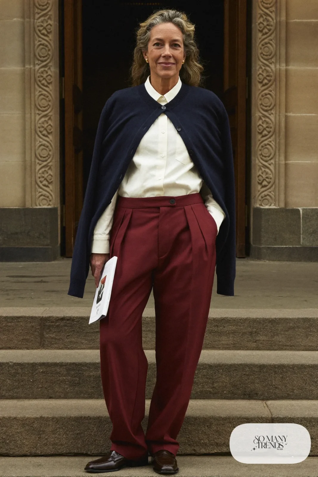 Woman over 50 in an ivory poplin shirt, oxblood wide-leg pants, navy cardigan and brown loafers, Christmas outfit 25