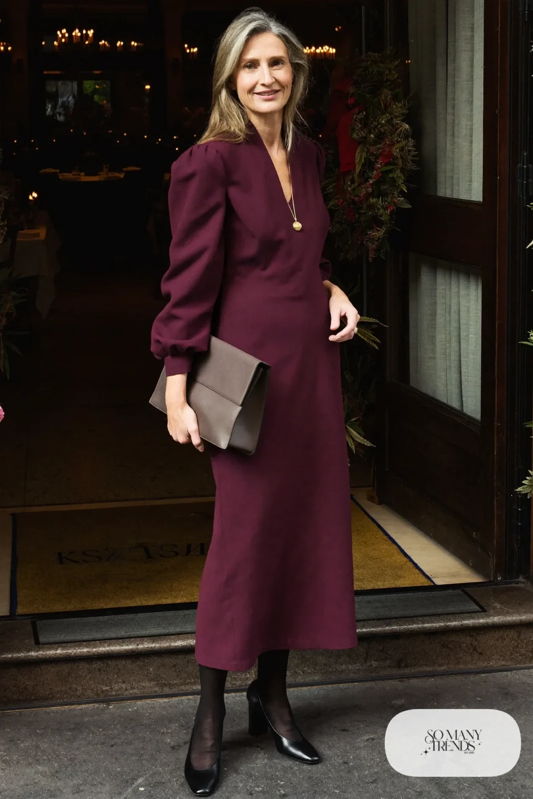 Woman over 50 in a plum midi dress, gold necklace, sheer black tights and black pumps, Christmas outfit 30