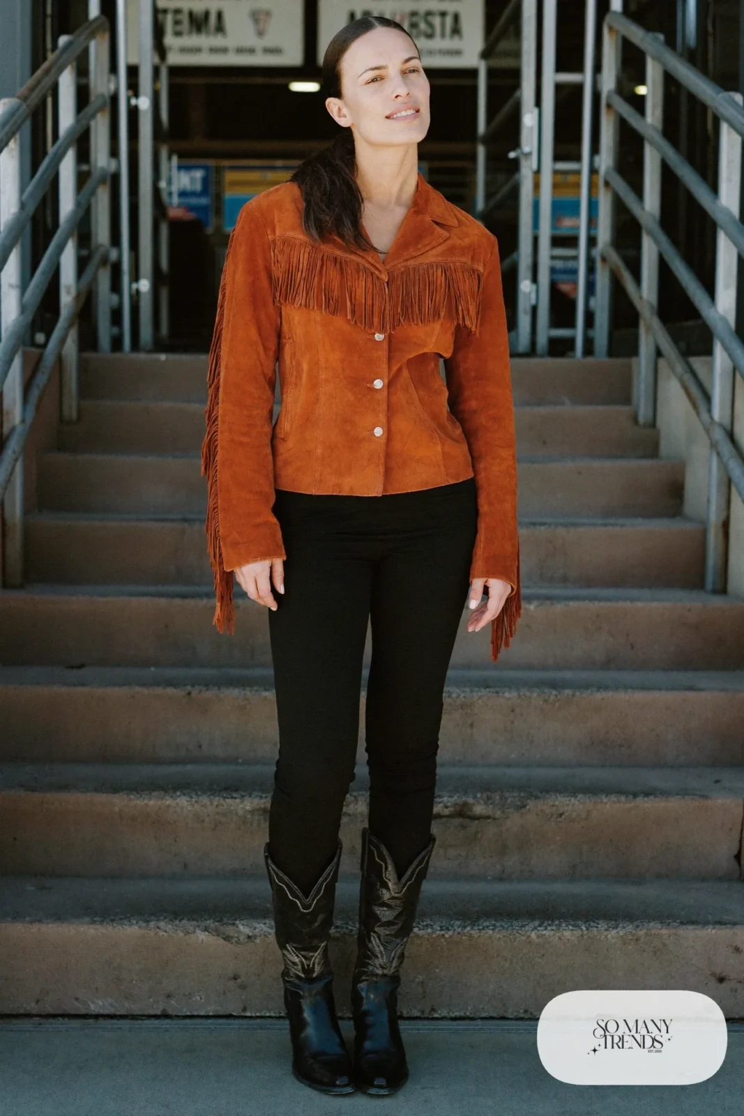 Woman in a rust fringe suede jacket, black slim pants, black knit top and black cowboy boots, outfit 3