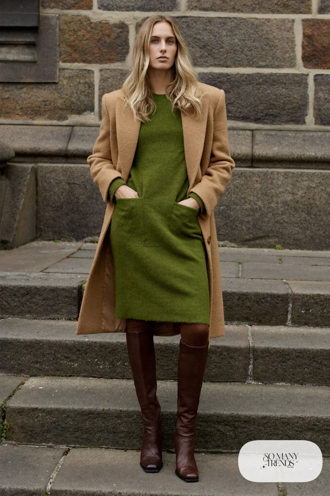 Woman in a moss green wool midi dress, sheer black tights, tall brown leather boots and a long camel coat open at the front at a castle, outfit 9