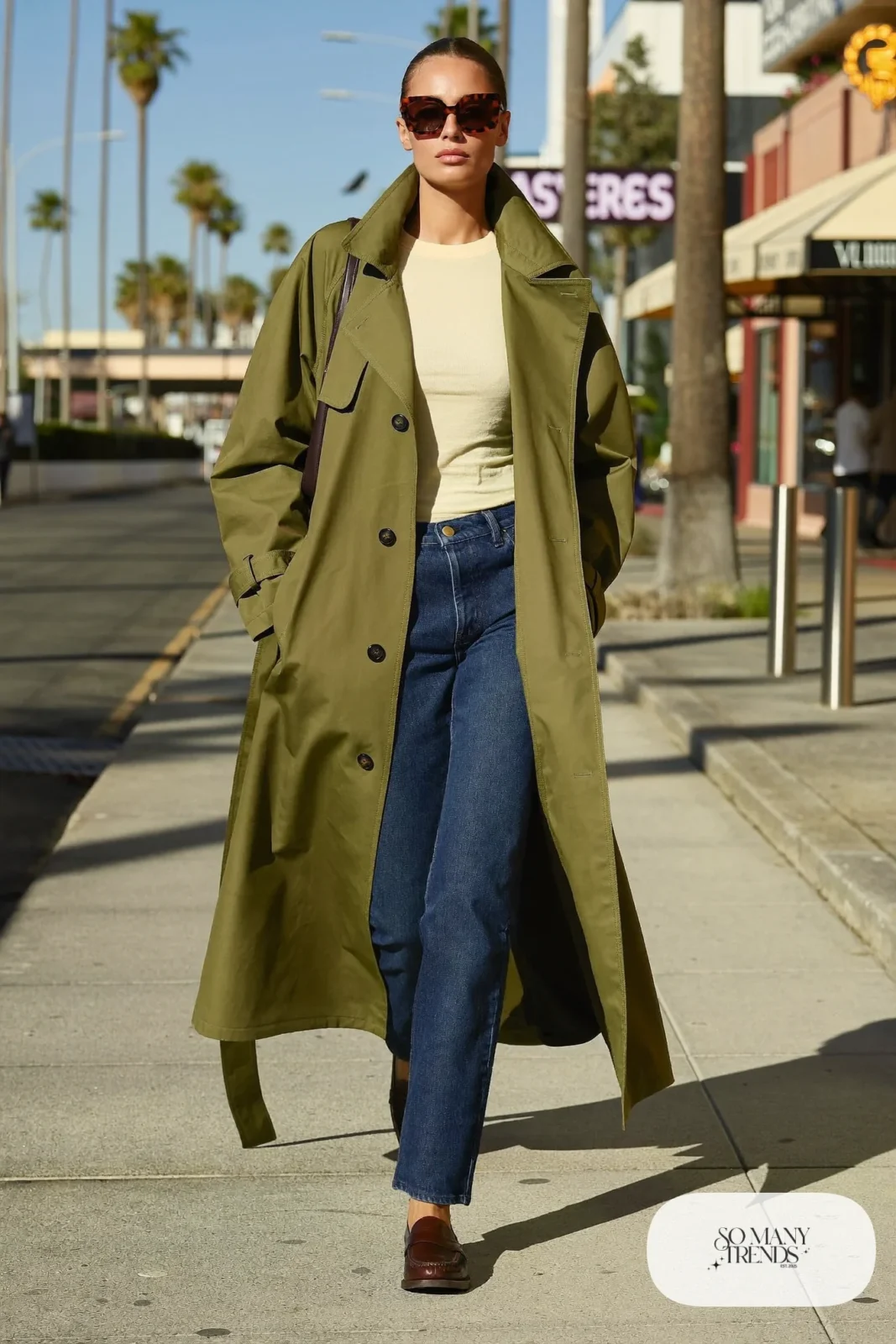 Woman in an olive trench coat, cream tee, indigo straight jeans and brown loafers in Las Vegas, outfit 5