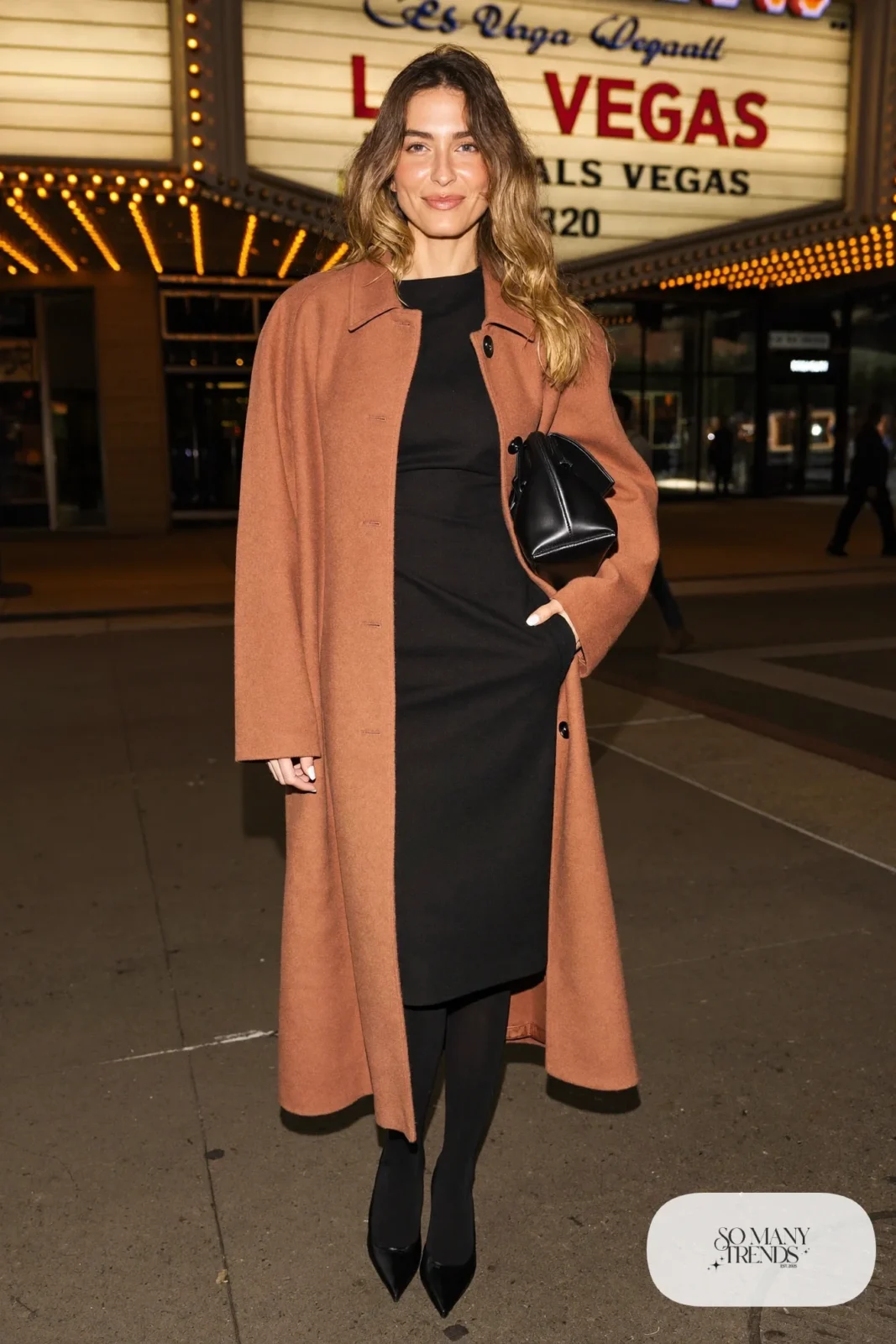Woman in a black column dress, terracotta wool coat, sheer black tights and pointed pumps outside a Las Vegas theater, outfit 7