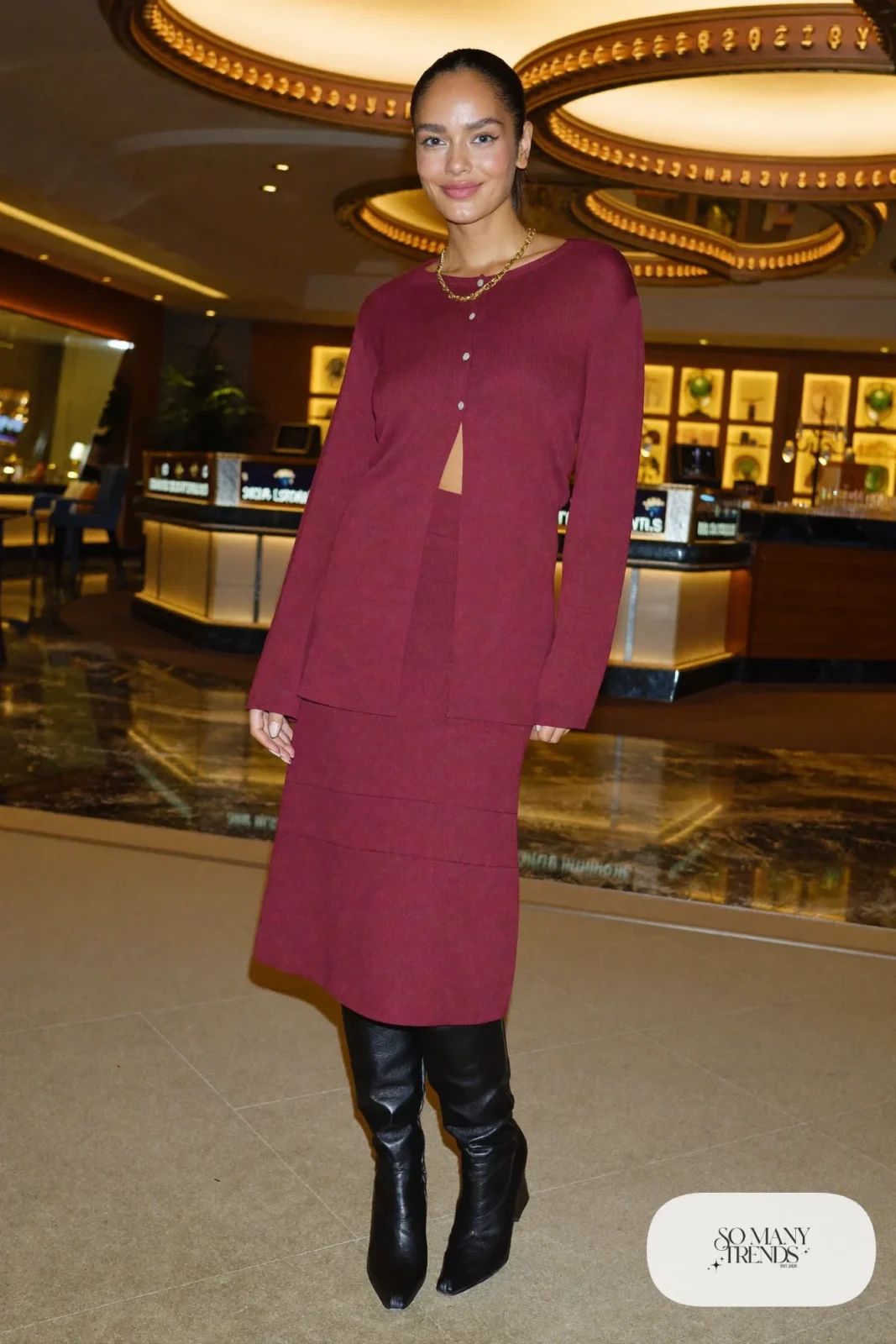 Woman in a burgundy knit cardigan and midi skirt set with tall black boots in a Las Vegas casino, outfit 15