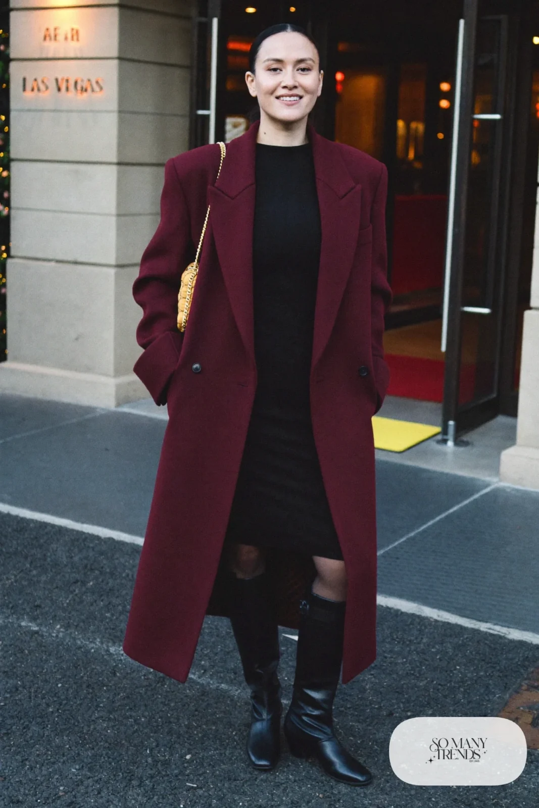 Woman in a long burgundy wool coat, black knit midi dress and tall black boots in Las Vegas at night, outfit 23
