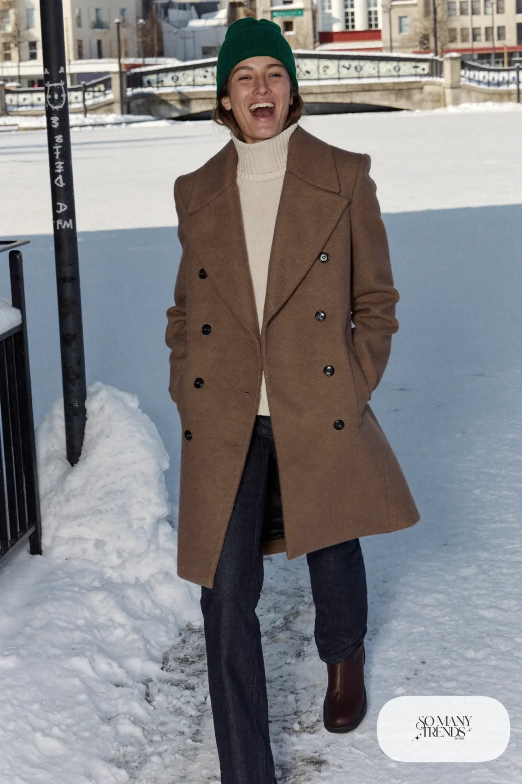 Look 2: camel double-breasted peacoat over a cream turtleneck and dark straight jeans with chocolate boots, snowy lakeside path