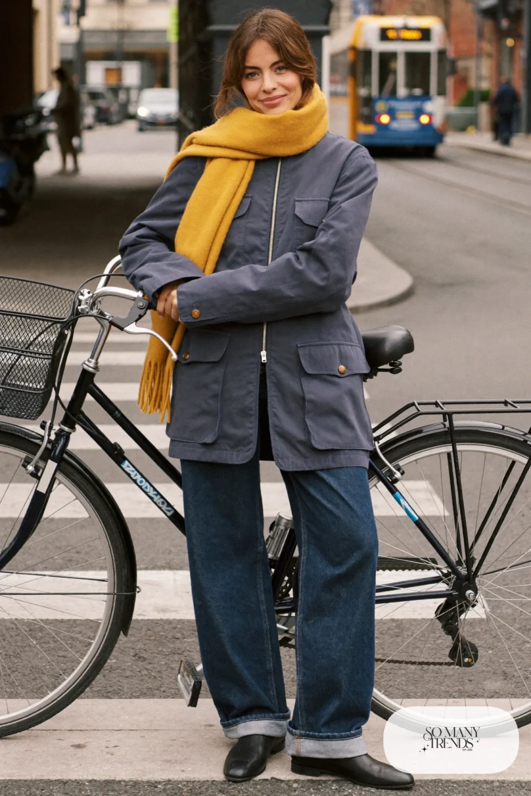 Woman in a navy utility jacket, ivory sweater, wide-leg dark jeans cuffed, black boots and mustard scarf by a bicycle, outfit 16