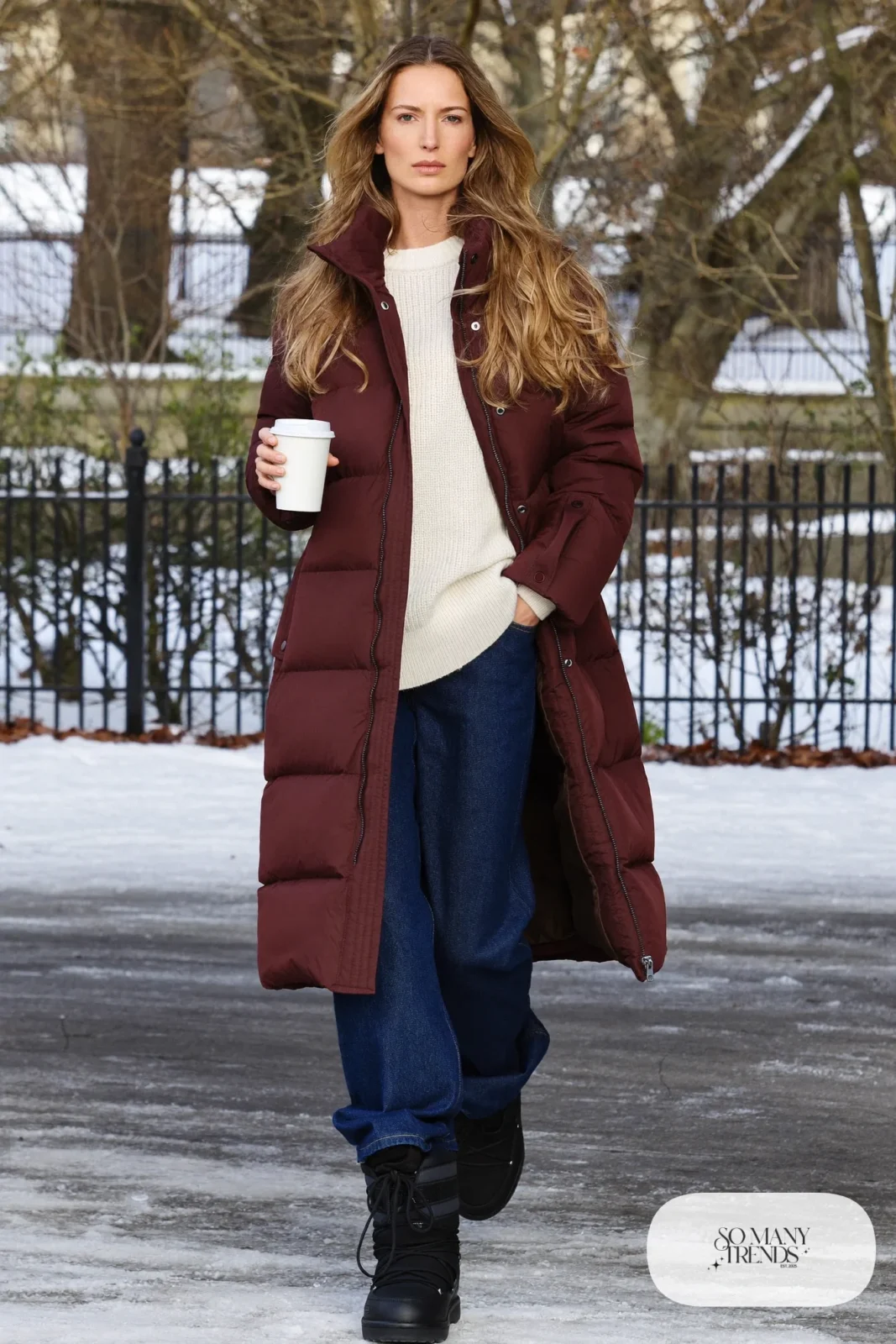Woman in a long burgundy puffer coat, cream sweater, dark straight jeans and black Sorel boots, outfit 2
