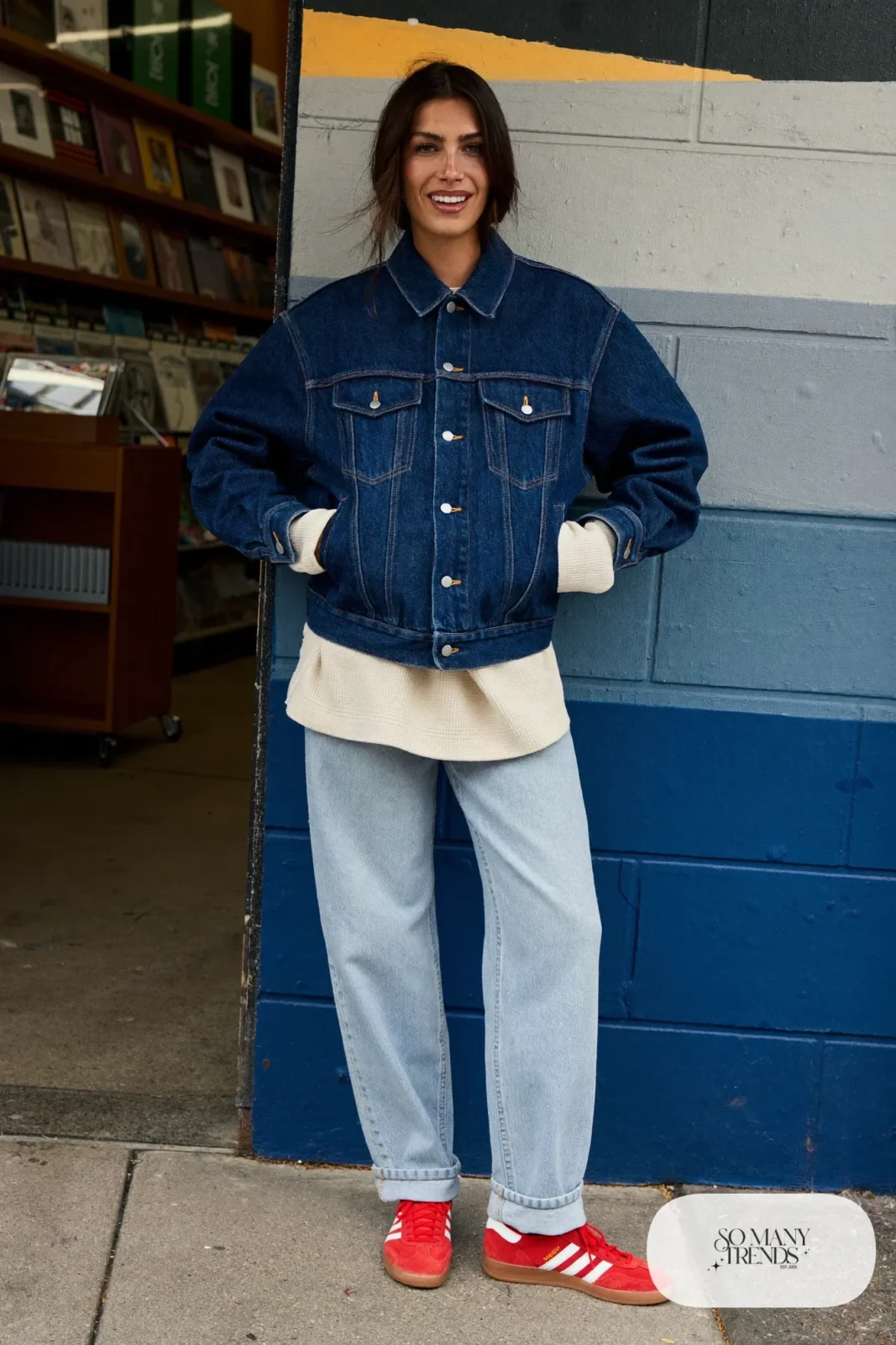 Woman in a dark denim trucker jacket, cream thermal top, light wash straight jeans and red Adidas Gazelle sneakers, outfit 4