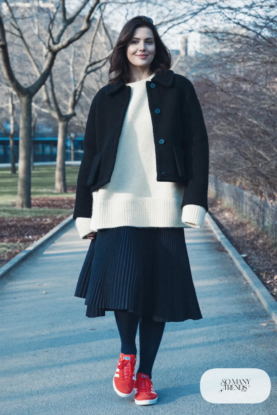 Woman in a navy pleated midi skirt, cream chunky sweater, navy opaque tights and red Adidas Gazelle sneakers, outfit 13