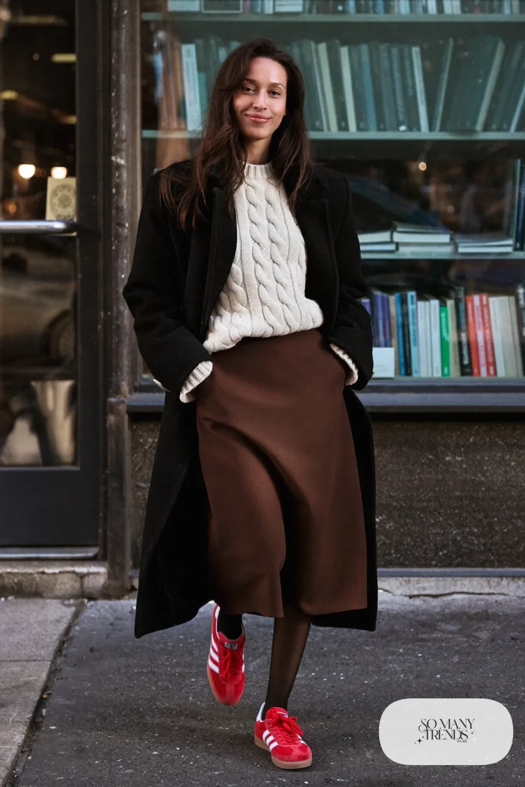 Woman in a chocolate brown fluid midi skirt, chunky cream cable sweater, sheer black tights and red Adidas Gazelle sneakers, outfit 17