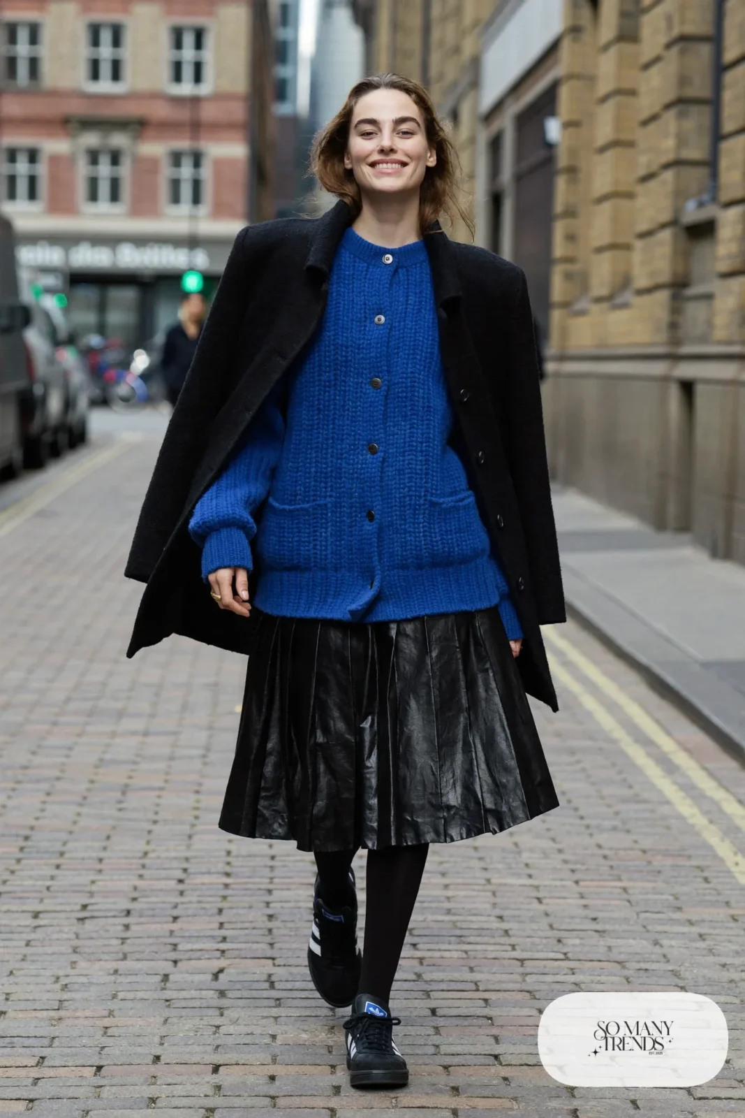 Woman in cobalt blue chunky cardigan, black pleated midi skirt, black tights and black Adidas Campus sneakers, outfit 7