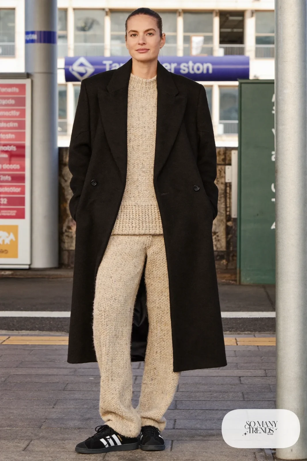 Woman in oatmeal knit sweater and wide knit pants set, long black coat and black Adidas Campus sneakers, outfit 26