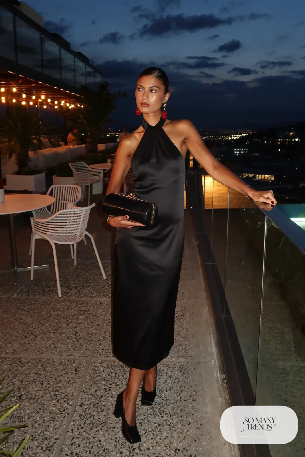 Woman in a black halter midi dress with red drop earrings and black block heels, look 9