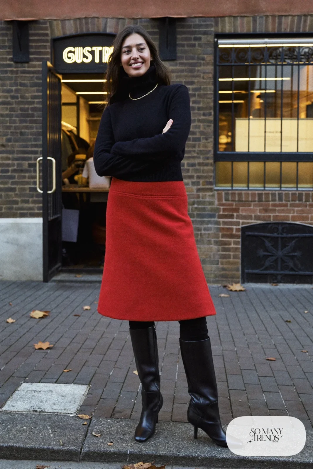 Woman in a red wool A-line skirt, black turtleneck and tall black boots, look 24
