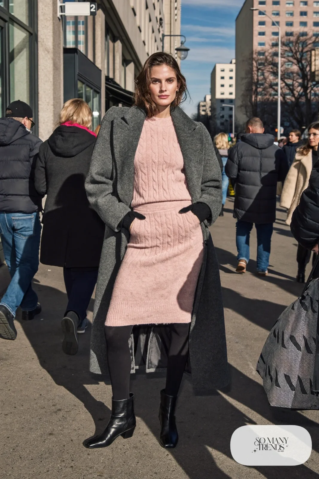 Woman in a blush pink knit sweater and midi skirt set, long gray overcoat, dark gray tights and black boots, outfit 5