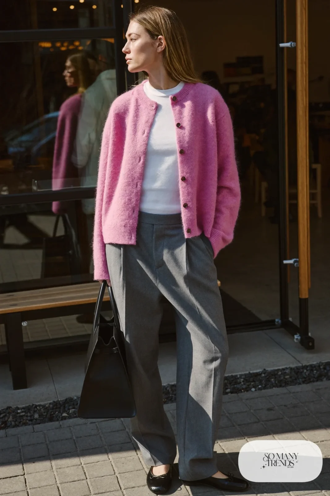 Woman in a pink knit cardigan, white tee, gray pleated pants and black flats, carrying a structured bag, outfit 6