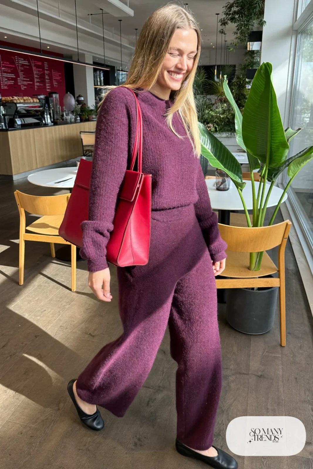Woman in a plum ribbed knit top and matching wide knit pants with black flats and a red leather bag, look 6