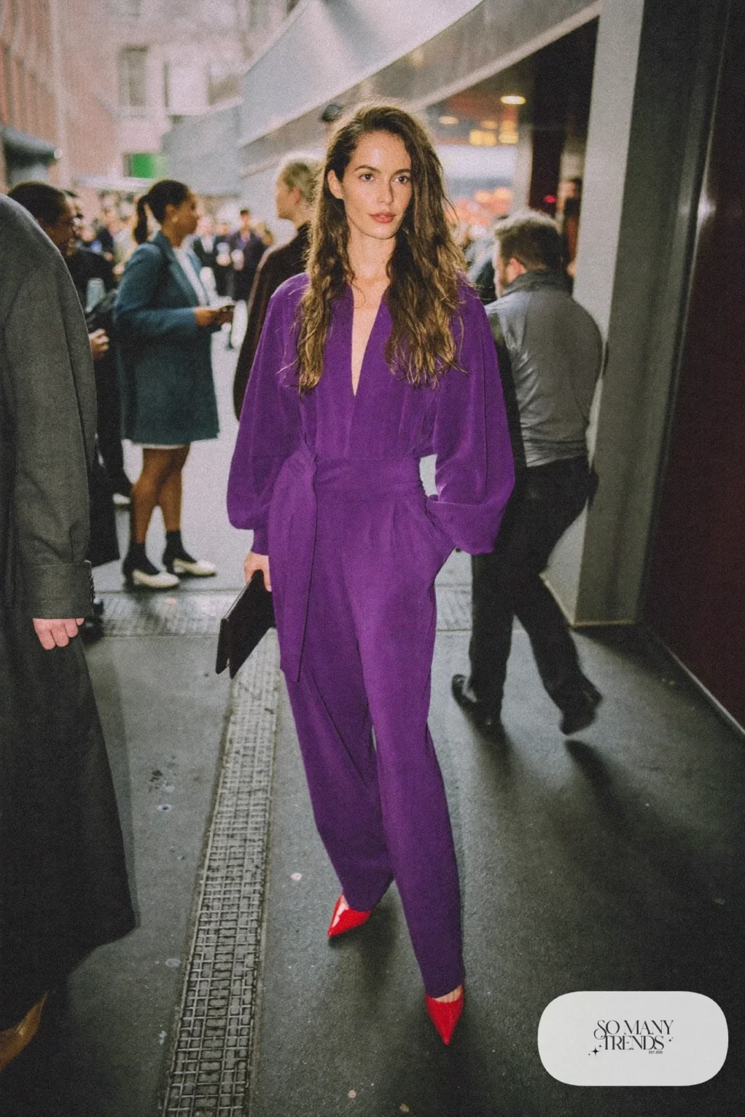 Woman in a violet wide-leg jumpsuit, red pointed heels and a small black bag, look 14