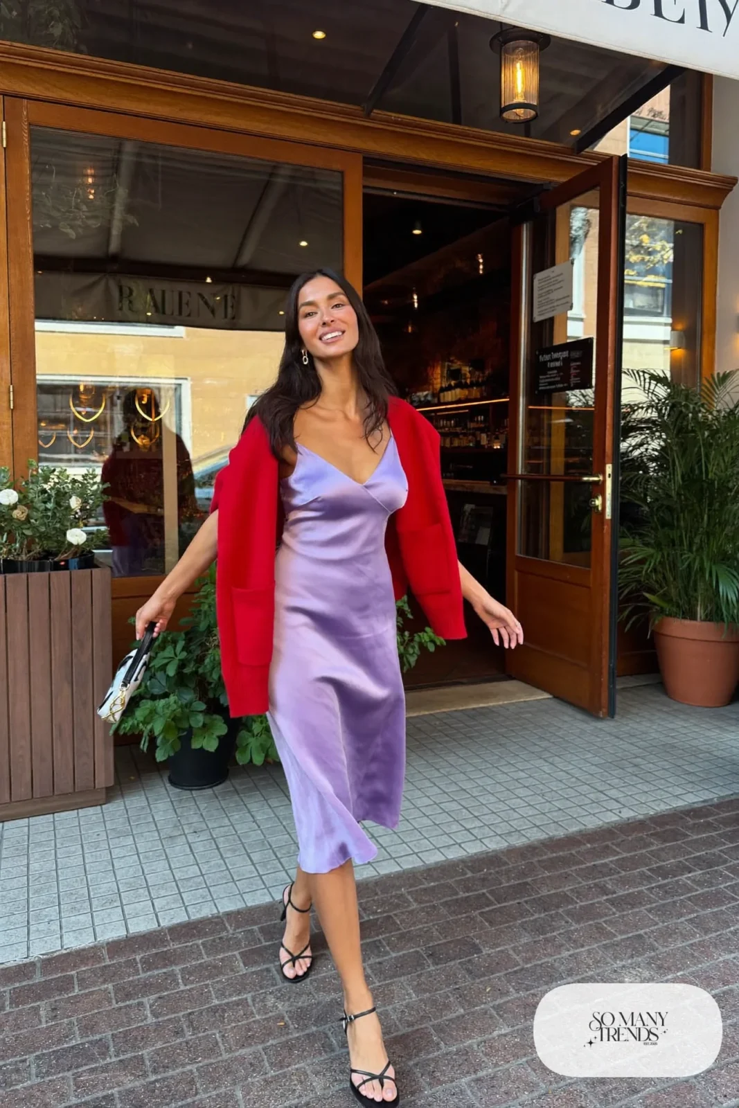 Woman in a lilac slip midi dress, red cardigan on the shoulders and black strappy sandals shown with bare legs, look 16