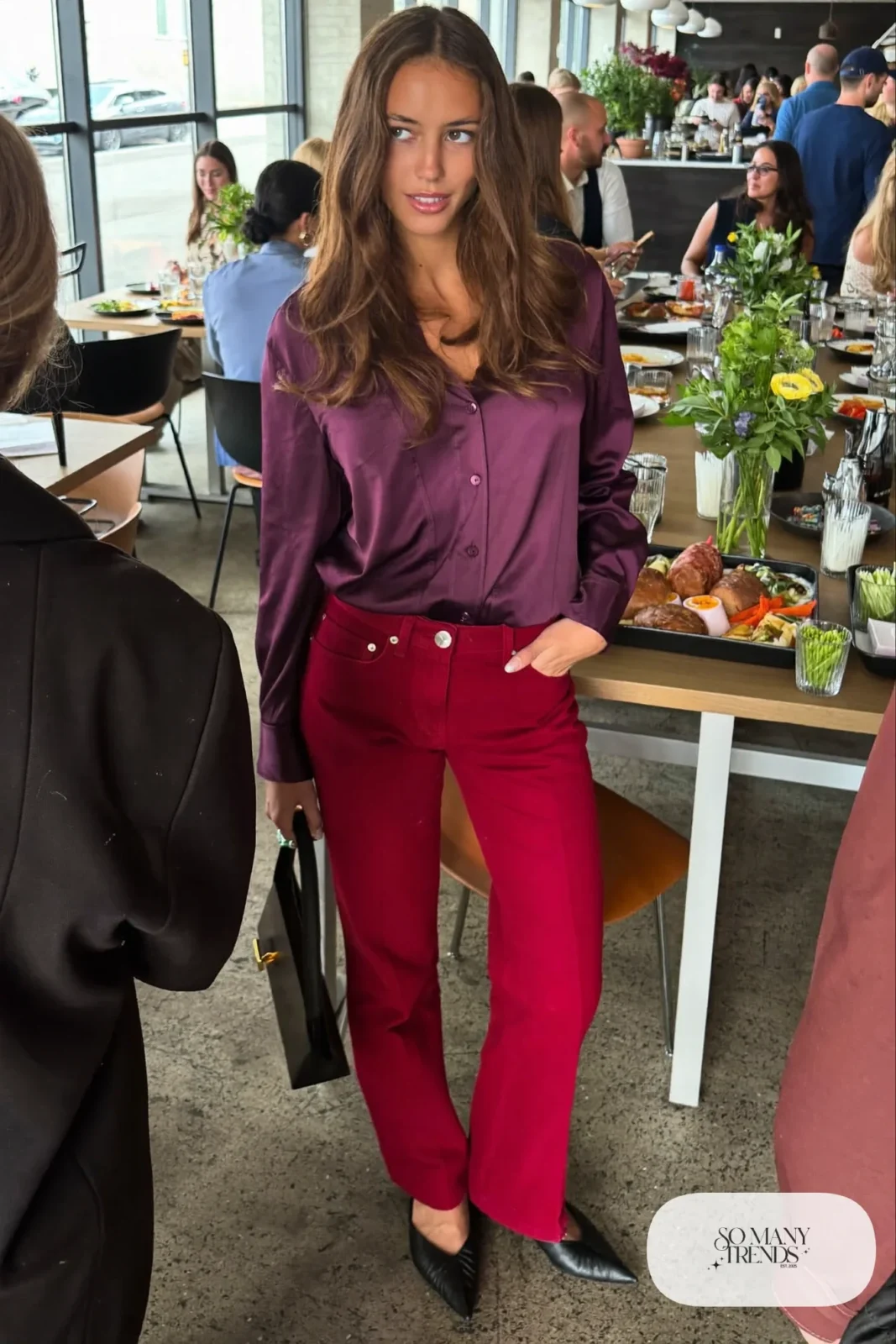 Woman in a plum satin blouse, red straight jeans and black pointed flats, look 22