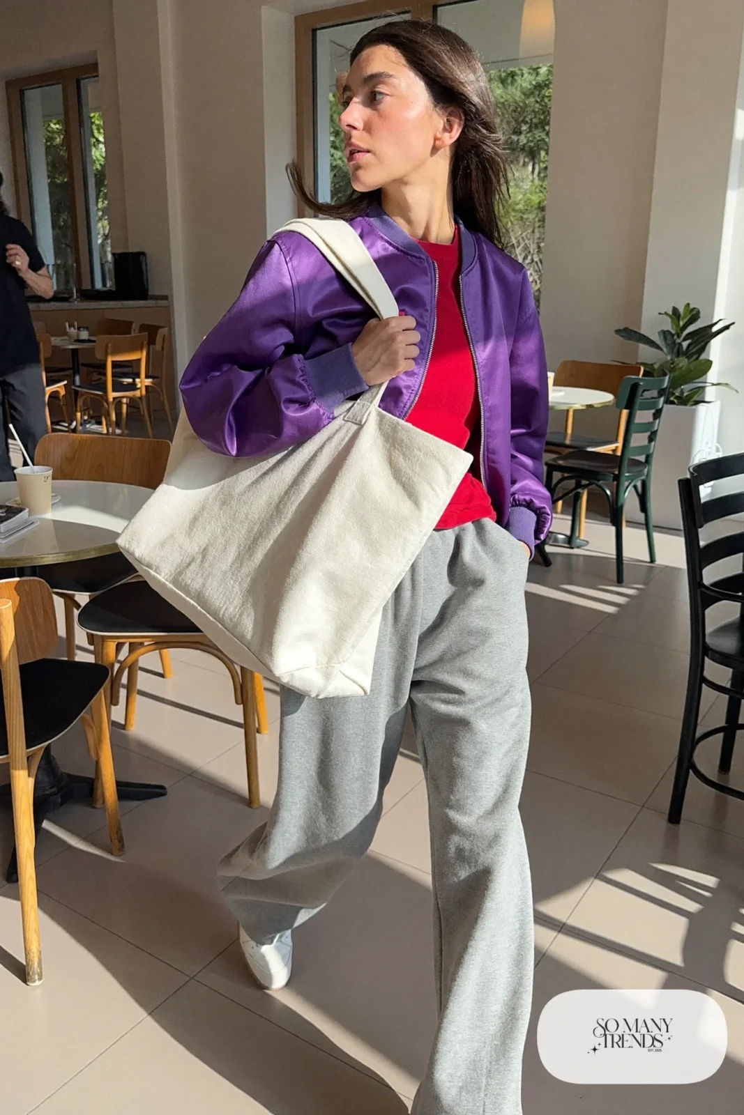 Woman in a violet bomber jacket, red tee, gray wide pants and white sneakers, look 23