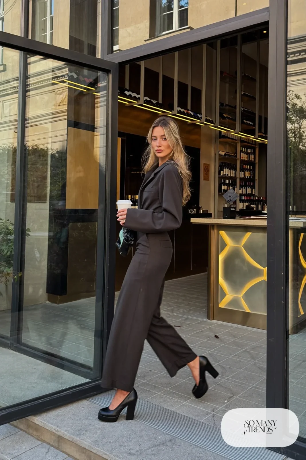 Woman in a charcoal wide-leg jumpsuit with black platform pumps and a bag, outfit 3