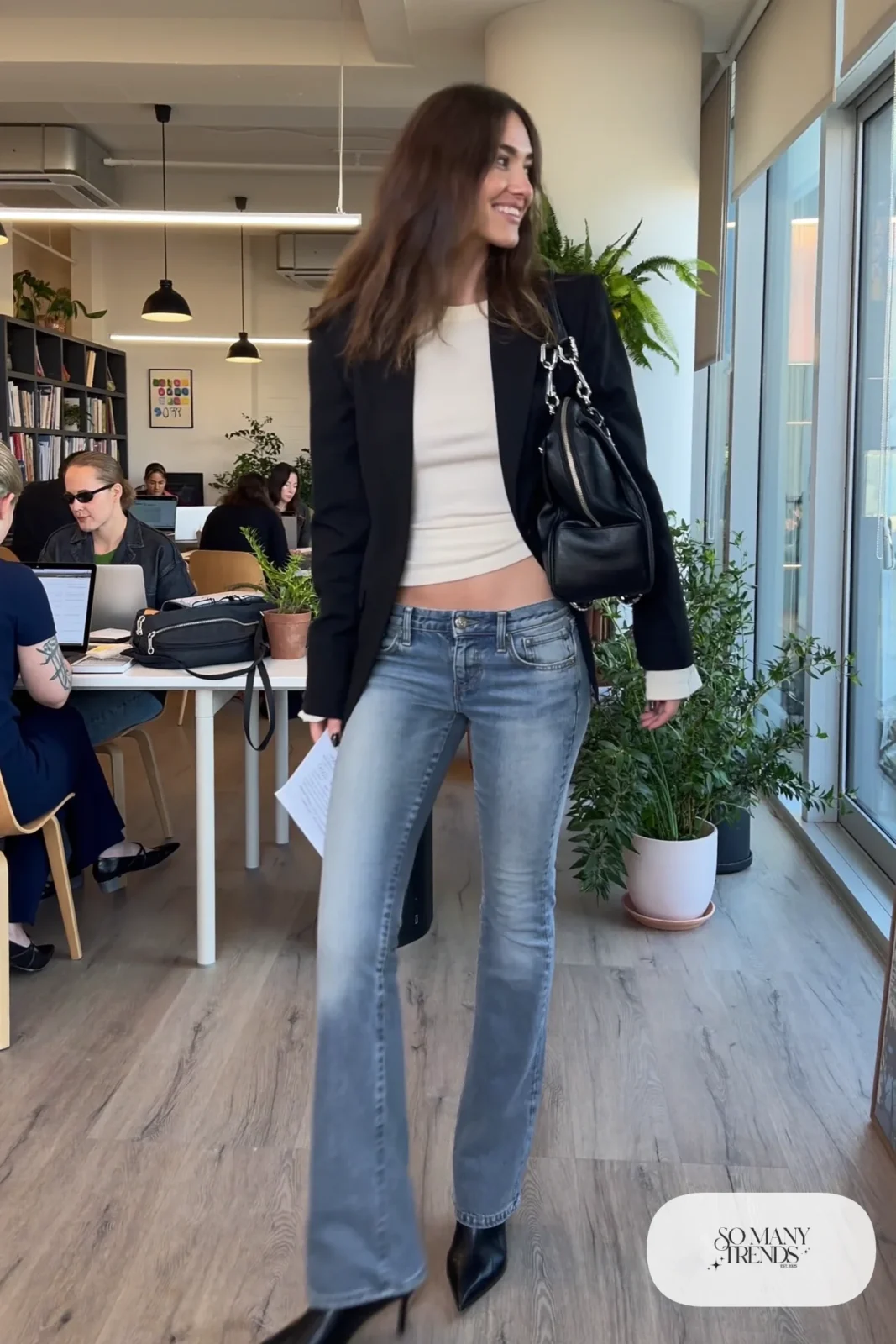 Woman in a slim black blazer, fitted ivory tee, low-rise light wash flare jeans and black pointed ankle boots, look 12