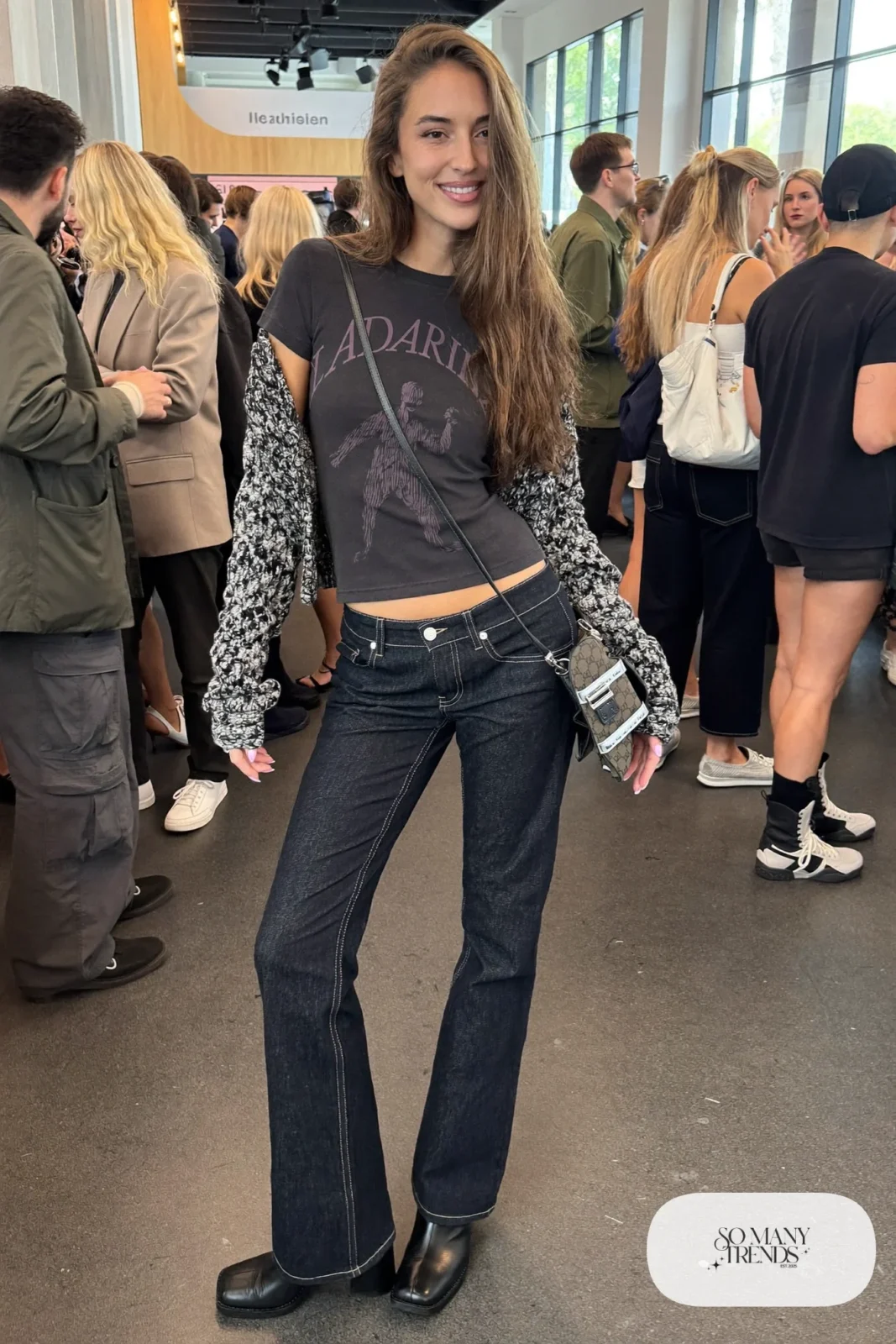 Woman in a faded black graphic tee, open gray cardigan, low-rise dark flare jeans and black block heel ankle boots, look 13