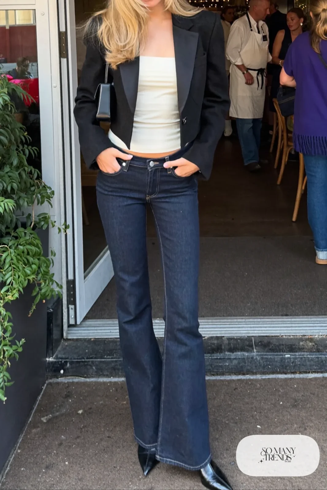 Woman in a black blazer, fitted ivory cami, low-rise dark flare jeans and black pointed heeled ankle boots, look 21
