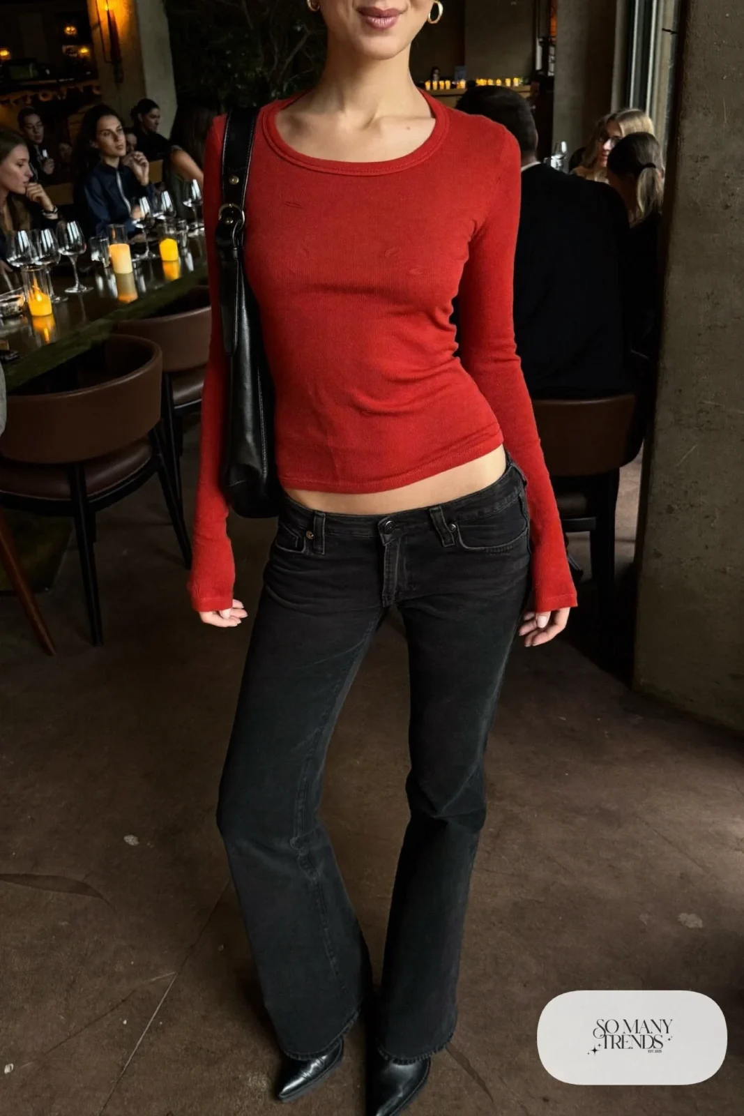Woman in a fitted tomato red scoop-neck knit top, low-rise black flare jeans and black pointed boots, look 22