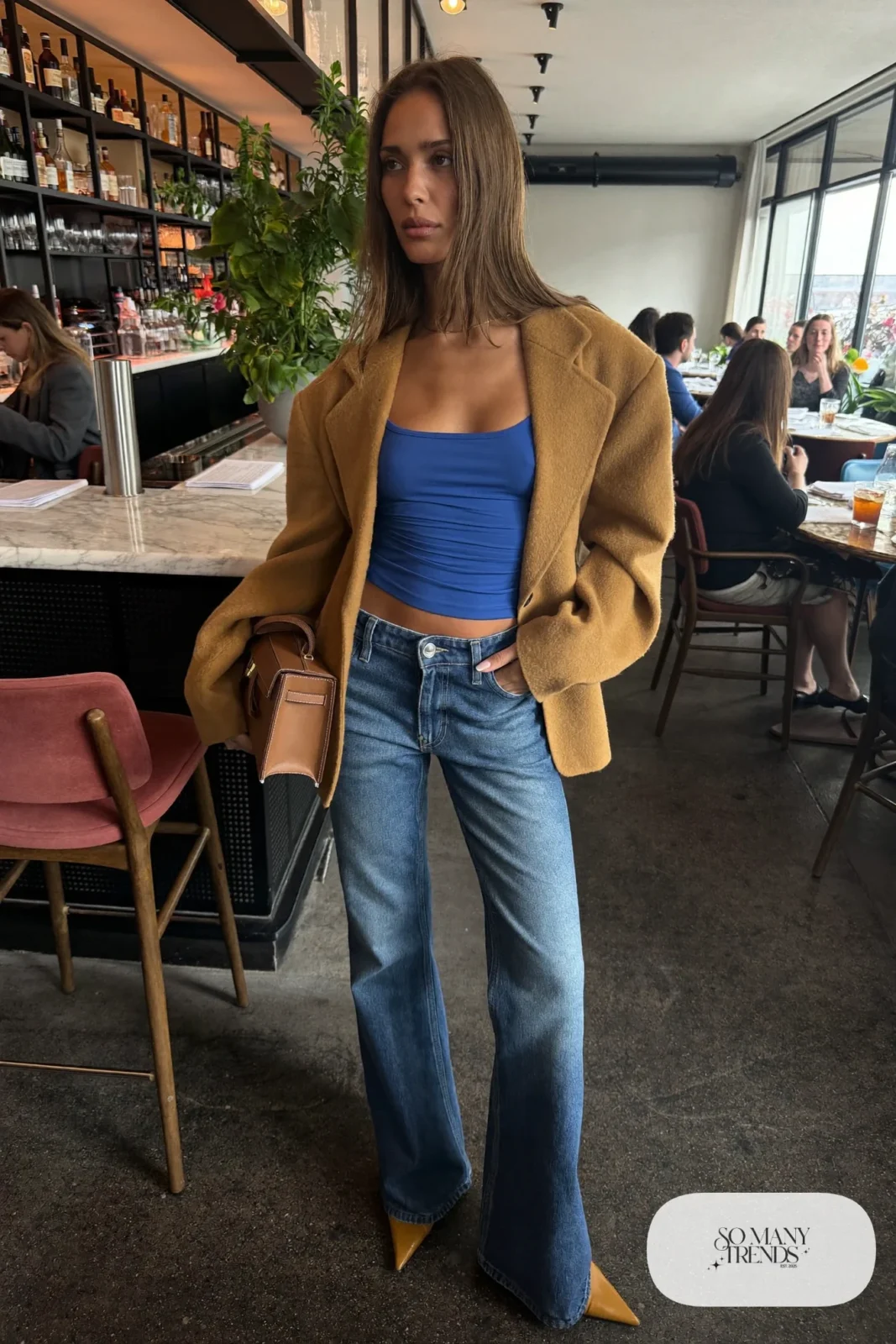 Woman in a camel blazer, fitted cobalt tank, low-rise medium-dark flare jeans and tan pointed heels, look 23