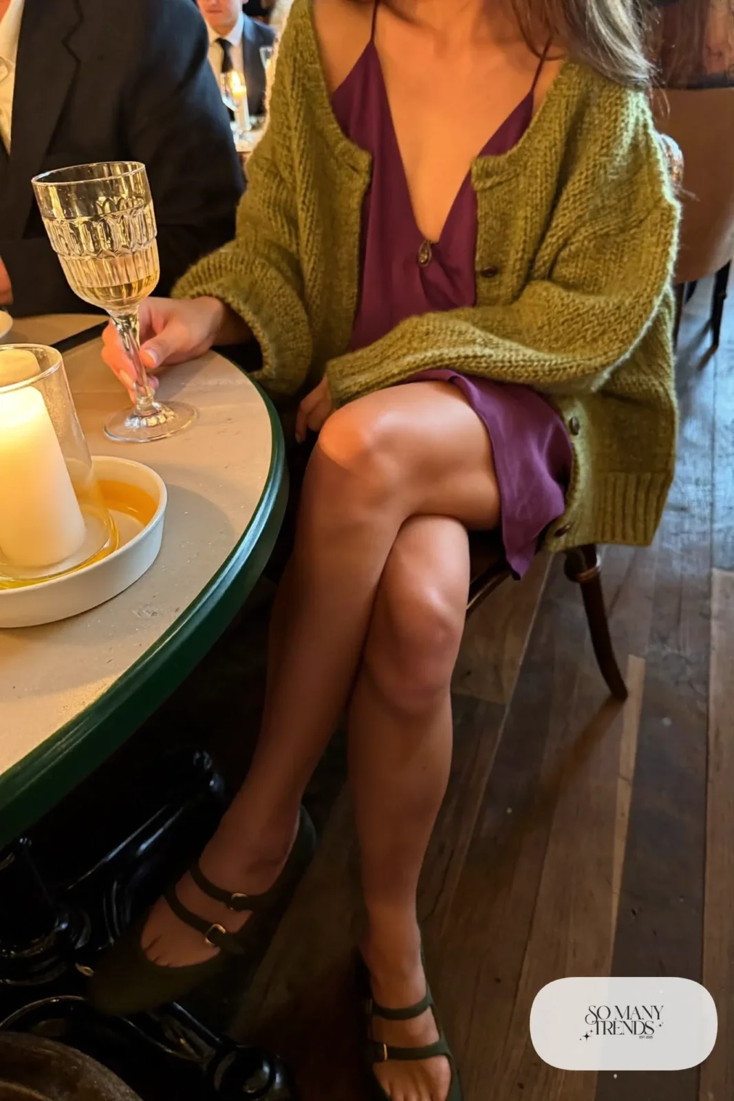 Woman in a plum slip dress, olive green cardigan and strappy flats at a restaurant table, outfit 4