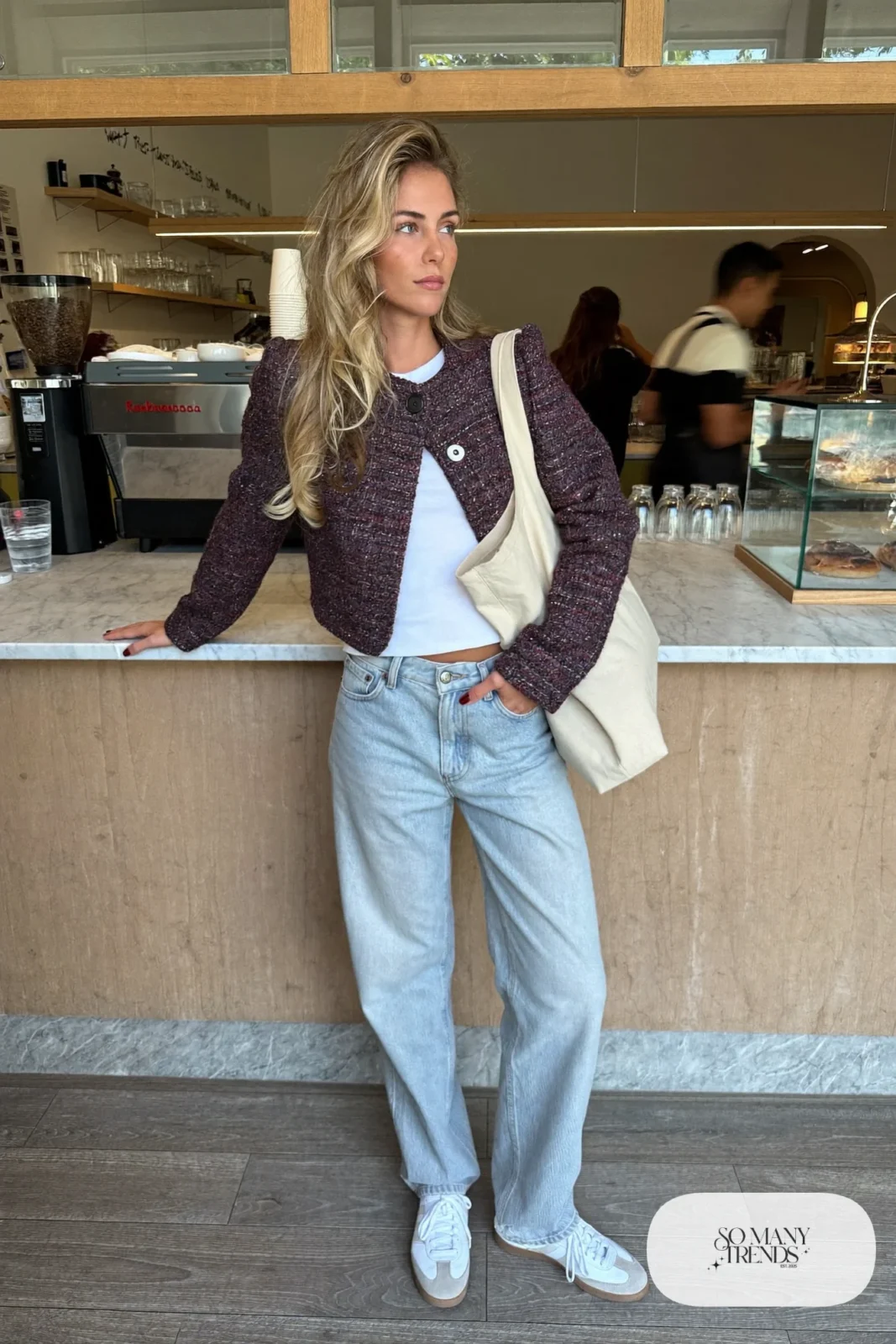 Woman in a short aubergine tweed jacket, white tee, light wash straight jeans and white sneakers at a cafe, outfit 18