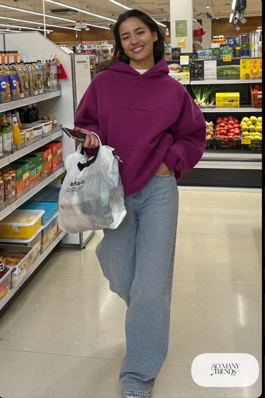 Woman in an eggplant hoodie, wide light wash jeans and white sneakers at a grocery store aisle, outfit 24