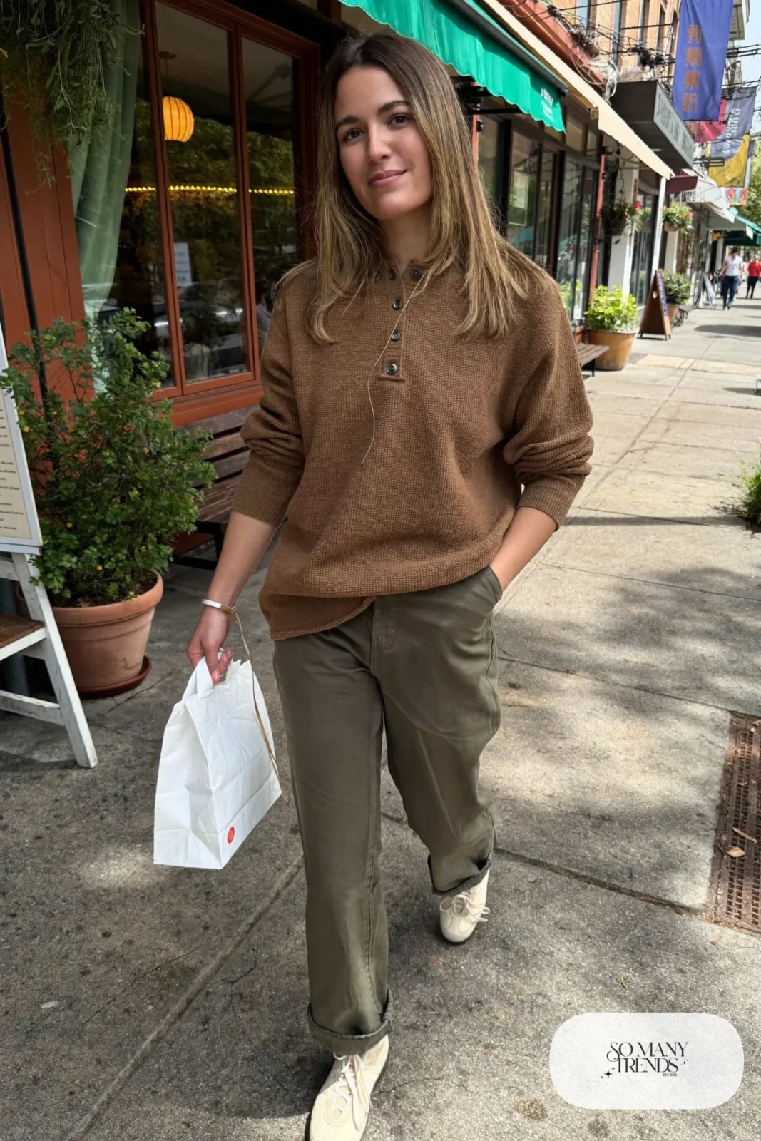 Woman in a camel henley, cuffed olive pants and cream sneakers, outfit 12